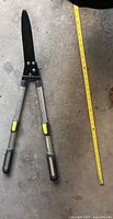 Photo of two extendable handle yard trimmers laid flat on concrete floor with measuring tape showing length.