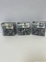 Three clear plastic boxes filled with new silver roofing screws with hex washer heads and white rubber washers.