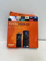 Front view of the orange retail box showing the Amazon Fire TV Stick Lite with Alexa Voice Remote and supported streaming services icons.