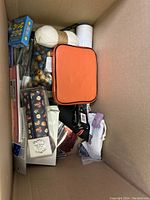 Photo of various miscellaneous craft and accessory items inside a cardboard box, including yarn, beads, pouches, and stationery.