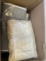 Photo of box containing cream fringed textile and dark fabric items in plastic wrapping