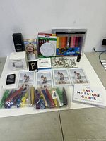 Photo shows all items arranged on white surface including baby milestone cards in frames, colorful pens, tubes, color palette, and small boxed items.