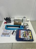 Photo showing assorted new items on white floor including manual pump, sprinklers, cartridges, and tarp.