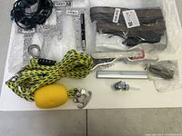 Overview showing nylon rope with clip and float, bungee cords in plastic, laser pointer pen, metal brackets, tap adapter, and black plastic components scattered on a white surface.