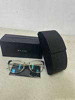 Prada optical glasses with case, box, and cleaning cloth displayed on a surface.