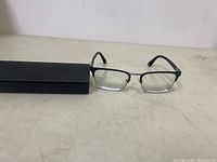 Front view of Prada rectangular glasses with black frame and black hard case in background.