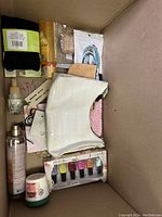 Overview of beauty and accessory items in box, including nail polish set, textured handbags, and body spray