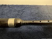 Close detailed view of the blackwood chanter showing the metal band and some faint markings on the wood.