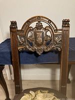 Close-up of the carved wooden backrest showing intricate detailing including a central shield crest and floral designs on each side.
