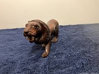 Front angled view of small carved rosewood lion figurine on dark fabric background.