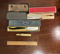 Lot items arranged with original boxes: two razors, sharpening stone, razor blade dispenser with ruler for scale