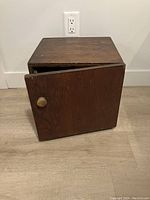 Closed view of a small wooden cupboard with a single door and round knob.