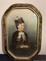 Full front view of painted photograph of woman in ornate frame, showing detailed decorations on frame and posture of subject