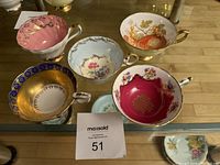 Five assorted vintage bone china tea cups arranged on glass surface with good lighting showing variety of colors and patterns