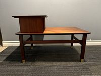 Front view of walnut side table showing stepped top shelf, brass capped legs, and wood grain