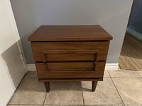 Front view of mid century modern walnut nightstand showing two drawers and tapered legs.