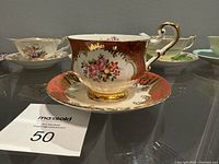 Fine bone china tea cup and saucer with red and gold floral pattern and ornate gold trim.