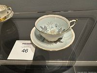 Fine bone china tea cup and saucer on glass surface with a floral design featuring blue flowers and gold trim, maker Paragon.