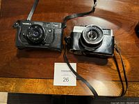 Full view of both vintage cameras, Yashica 35 MF on left and Sears Auto 800 in case on right, on wooden table showing overall condition and straps