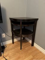 Photo showing the front and side view of the vintage dark wood corner table with built-in chair, highlighting the curved chair underneath the tabletop and overall structure.