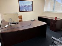 Full view of large dark wood office desk with curved front and matching side cabinet with three drawers in a modern office environment.