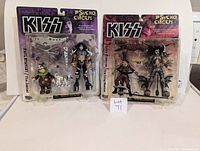 Two KISS Psycho Circus action figure sets in original packaging. One set includes Paul Stanley and The Goblin characters with accessories; the other set features Peter Criss and an alligator illustration-themed figure with accessories.