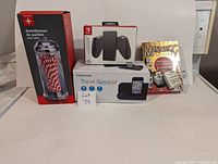 Mixed lot of items on white background including straw dispenser, Nintendo Switch controller grip, travel speaker, Mahjong cards, and dice game