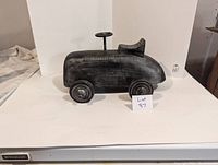 Front angled view of black wooden vintage pedal car showing overall shape and wheels on a white background.