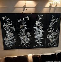 Four vertical black lacquer panels mounted on wall showing mother of pearl inlaid floral and butterfly designs.