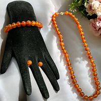 Photo showing entire jewelry set including carnelian stone necklace, bracelet on black display hand, and stud earrings on display fingers.