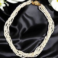 Front view of the vintage freshwater pearl multi-strand necklace laid flat on black satin fabric, showing pearl texture and gold-toned clasp detail.