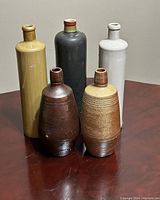 Overview of all five jugs including three tall German MKM wine jugs and two Portuguese salt glazed beer jugs on a wooden surface.