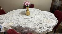 White Italian lace table cloth spread on table with floral centerpiece, showing intricate lace pattern and scalloped edges.