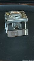Front angle view of square glass inkwell with closed sterling silver lid and push button.