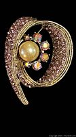 Close-up of the vintage lavender rhinestone swirl brooch featuring a central faux pearl and smaller iridescent rhinestones