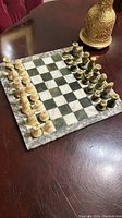 Photo of the marble chess board with pieces set up on one side showing white and black patterned squares and full chess pieces arranged.