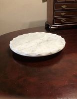 Side angle showing the full circular form and height of the thick white marble tray on a dark wooden surface.
