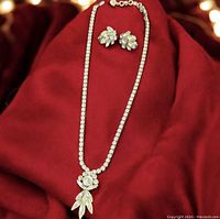 Full view of necklace and earrings on burgundy fabric background, showcasing rhinestone details and pendant design.