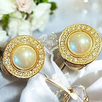 Close up photo of the front side of the vintage gold-tone clip on earrings with faux pearl centers and rhinestone halos.