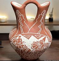 Front angle showing detailed white etched native figures and motifs on terracotta double-spouted wedding vase with central handle.