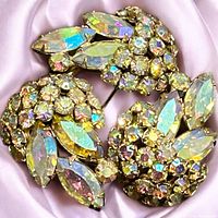 Close-up photo of signed Sherman brooch with aurora borealis rhinestones reflecting several colors on a pink cloth.