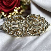 Close up of the ornate Swarovski crystal brooch on white satin showing detail and condition