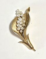 Front view of gold-tone calla lily shaped brooch with faux pearl cluster detail against a white background.
