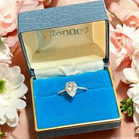 Close-up image of the sterling silver ring with pear cut clear stone in Monaco branded box with blue velvet interior and gold trim