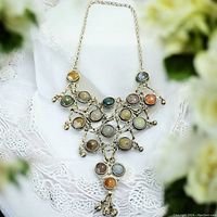 Full view of vintage bib necklace with multi-colored stone cabochons on white lace background.