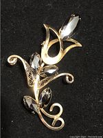 Front view of vintage gold filled floral brooch with black hematite stones on black background.