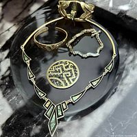 Full view of jewelry collection on black marble background, showing necklace, bracelets, brooch, and earrings clearly with abalone inlay details visible.