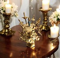 Photo of the Toledo Damascene hors d'oeuvres cocktail servers set on a wooden table surrounded by candle holders and decorative flowers. The set shows miniature sword handle servers in a two-tier brass stand with ornate etched designs.