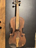 Top front view of an antique violin showing a worn wooden surface with no strings, missing or broken parts, and visible damage on the body edges.