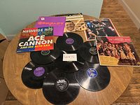 Nine vinyl record albums arranged on a wooden table, showing front covers of several albums and individual records off the sleeves.